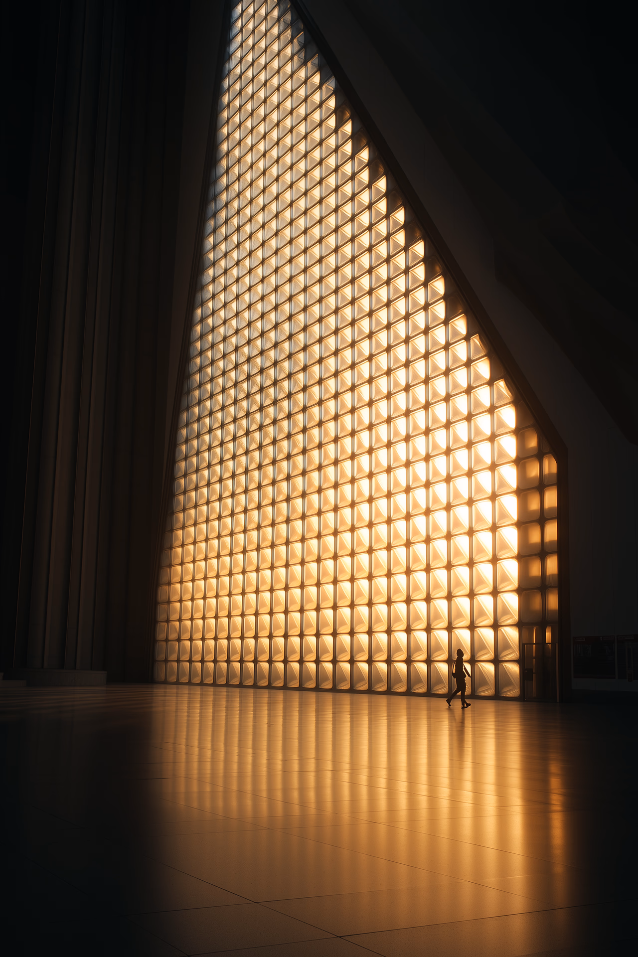 photography, triangular pattern translucent glass wall installation with black metal frame grid, warm golden backlight creating honeycomb shadows, silhouette of person walking, zen interior design style, amber glow atmospheric lighting, professional studio setup with two continuous led panels for backlight at 2800k, geometric repetitive patterns, high contrast interior shot, ultra sharp details, photorealistic quality, 48K resolution, rich detailing --ar 2:3 --quality 2 --style raw --sref 1009931265 --personalize c84qxg1 --stylize 400 --v 6.1