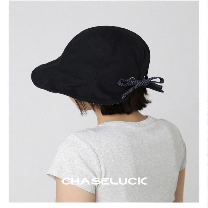 A young woman with a short bob haircut wearing a black bucket hat and a gray ribbed tee, stands in a minimalist white studio. Camera slowly orbits 180° from back three-quarter view to direct back view, highlighting the hat's clean rear panel stitching and adjustable black cord toggle. Soft, even studio lighting. Her shoulders relax naturally as she turns. Smooth, continuous motion. Premium fashion product videography. 8 seconds, seamless loop guided by the uploaded photo. In the final 2 seconds, space opens for text overlay (CHASELUCK). Clean beauty lighting, 4K, high-end fashion editorial aesthetic.