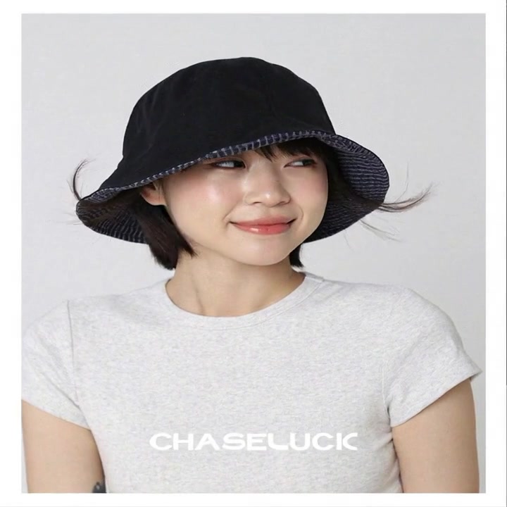 A relaxed Asian girl in a black bucket hat and a gray ribbed tee, standing against a minimal light gray backdrop. Natural daylight quality. A subtle breeze gently lifts her short black hair. She slowly turns her head from side profile toward camera with a soft, effortless expression. Shallow depth of field, organic motion, wearable everyday elegance. Seamless 8-second loop, guided by your uploaded photo. In the final 2 seconds, space opens for text overlay (CHASELUCK)."